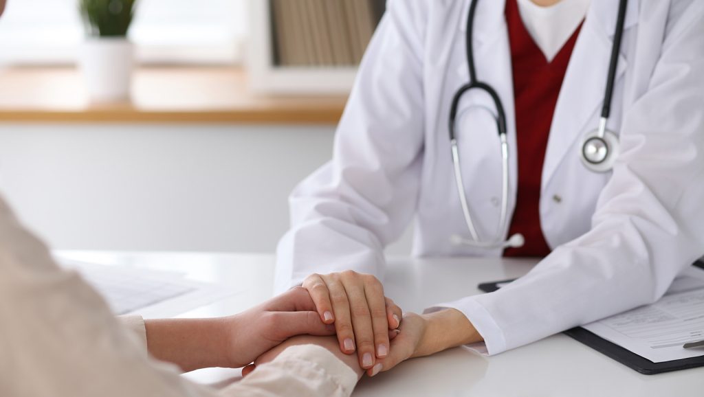 Doctor holding patient's hand discussing alternative views of cancer
