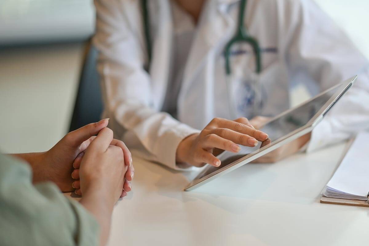 Doctor in white coat using tablet to discuss health information with patient, emphasizing patient care and navigating health systems.