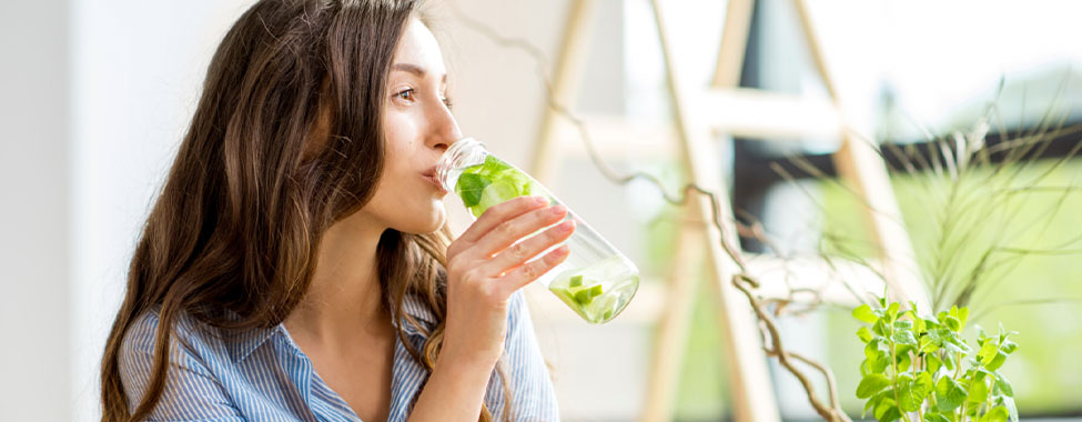 Woman drinking detoxifying water infused with herbs, promoting wellness and health benefits related to detoxification.