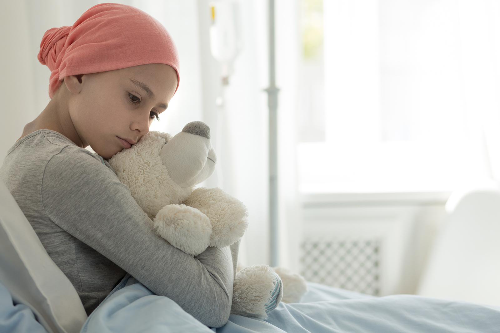 young cancer patient in bed holding a teddy bear during the war on cancer