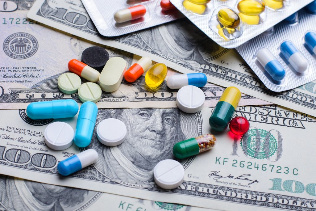 Colorful pills and capsules scattered on US hundred-dollar bills, illustrating the intersection of money and the pharmaceutical industry in health choices.